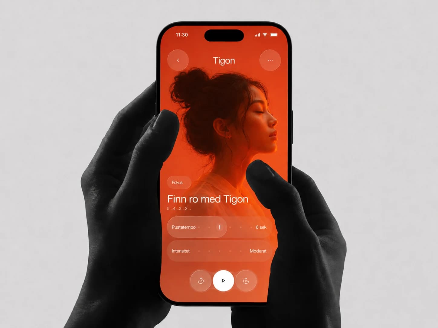 En hånd holder en smarttelefon med en oransje Tigon-app for meditasjon, fokus og pustetempo.