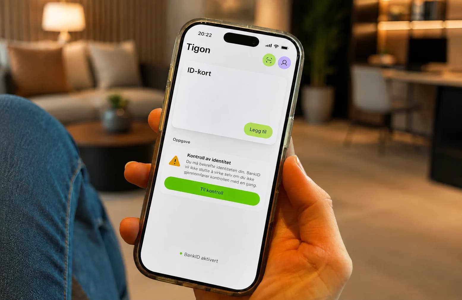Hånd holder en telefon med aktivert BankID og kontroll av identitet i en varm lounge