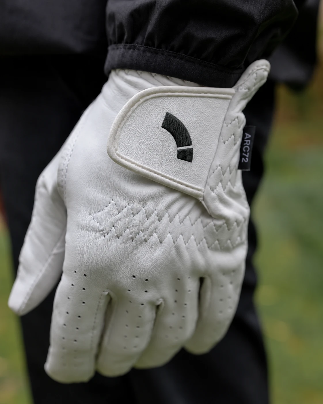 Hvit golfhanske med ARC72-symbolet brodert på borrelåsflappen.
